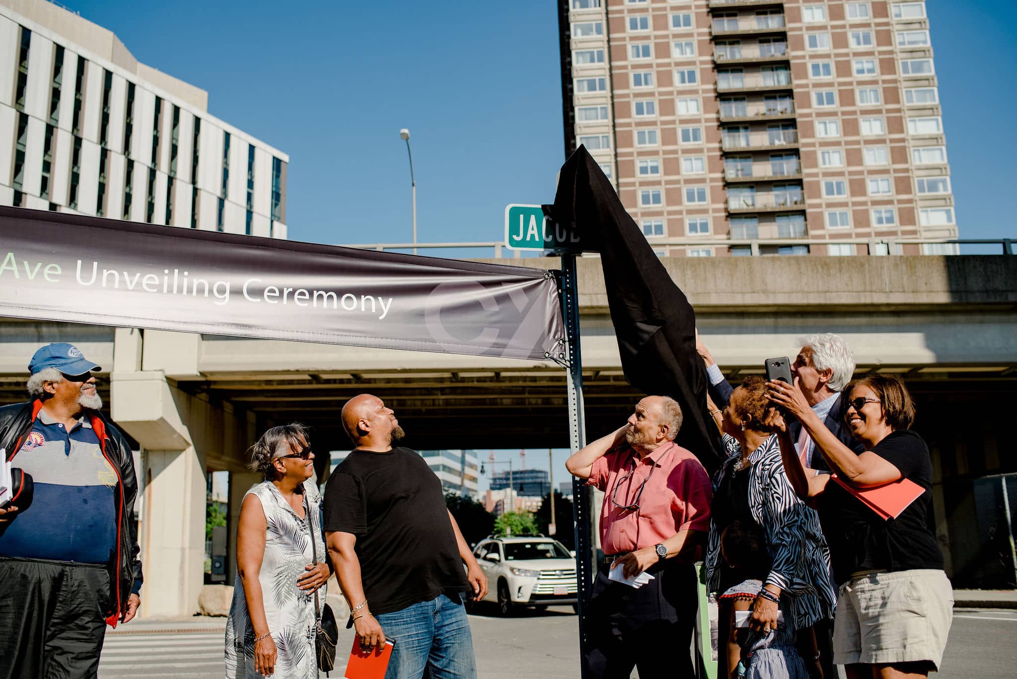 Group unveils new Jacobs Street sign during community ceremony under a clear blue city sky