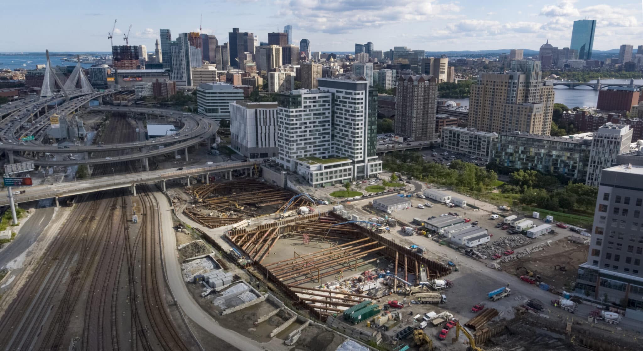 Wide-angle aerial of construction site amid Boston skyline, highways, and active rail lines