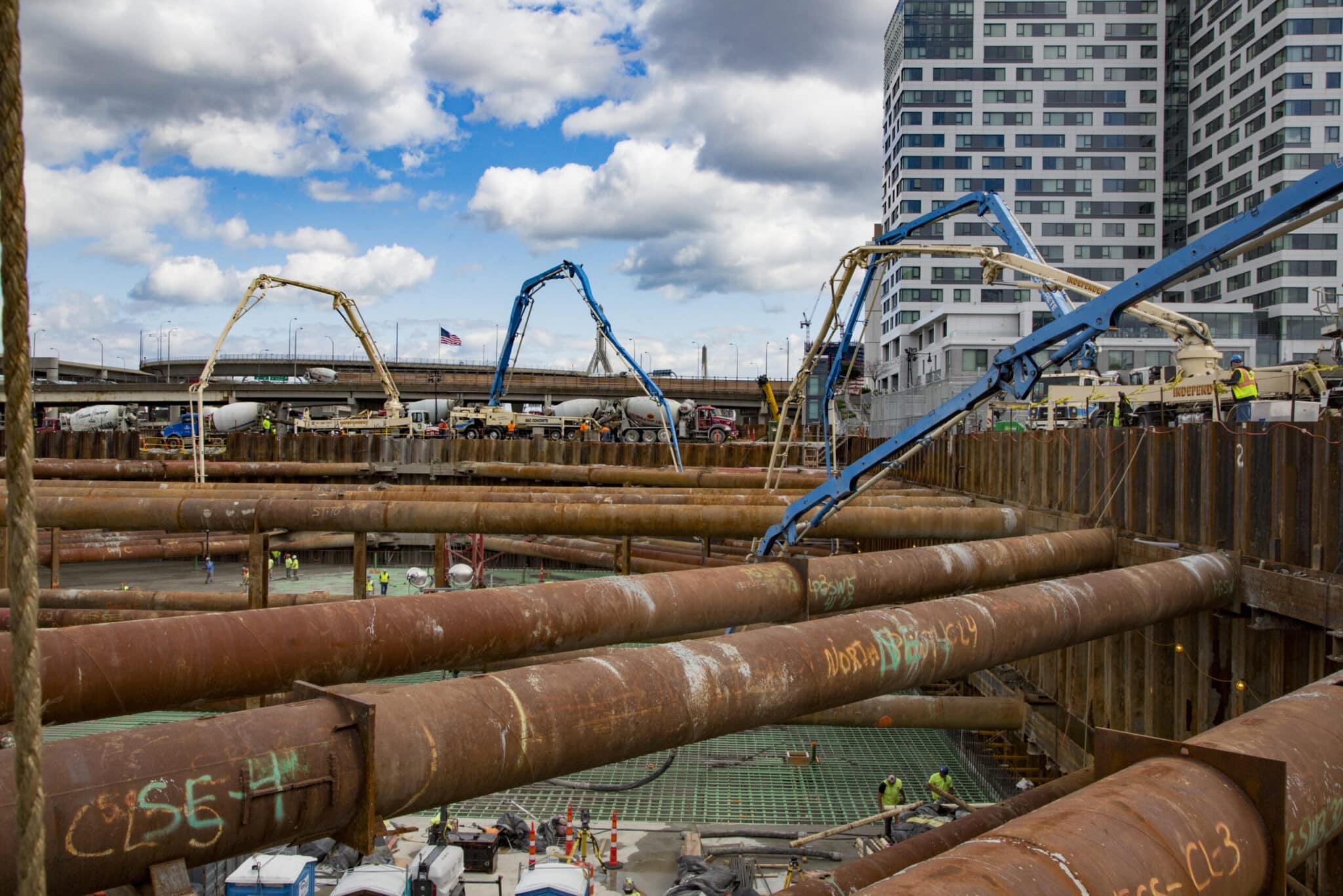 Foundation work with workers and concrete trucks surrounding rebar grid and retaining walls