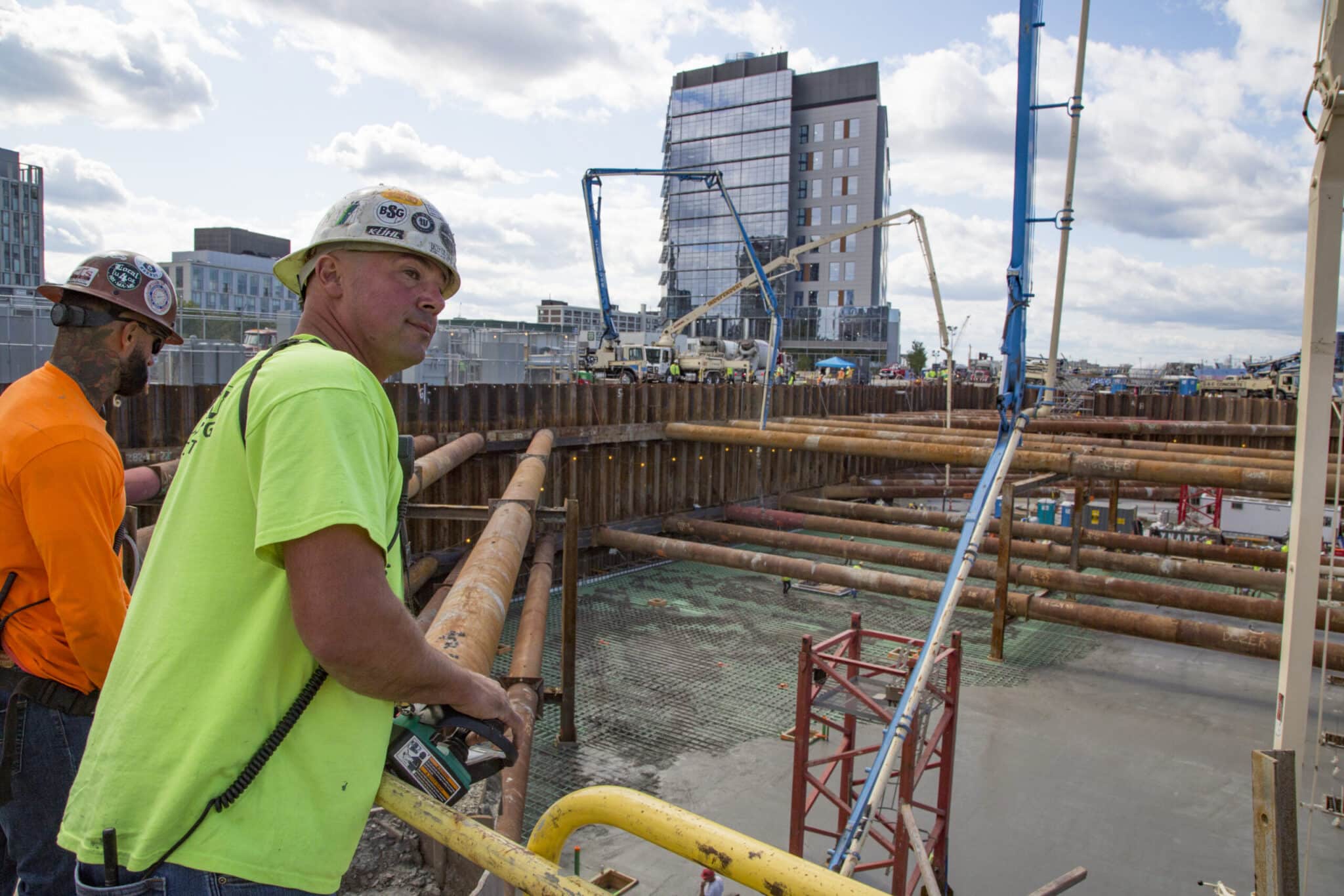 Construction foremen monitor progress as pump trucks deliver concrete into deep excavation zone