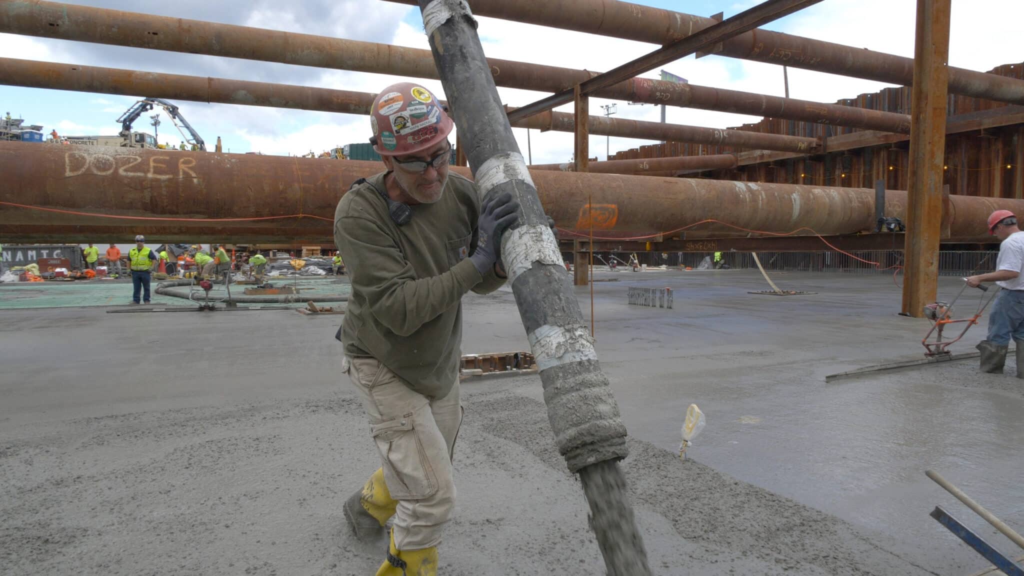 Construction worker directs concrete pouring using thick hose on large urban development site