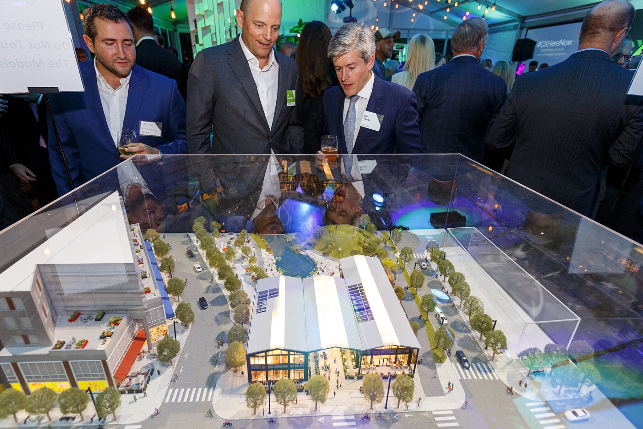 Guests in formal attire examine miniature Cambridge Crossing model at promotional display event