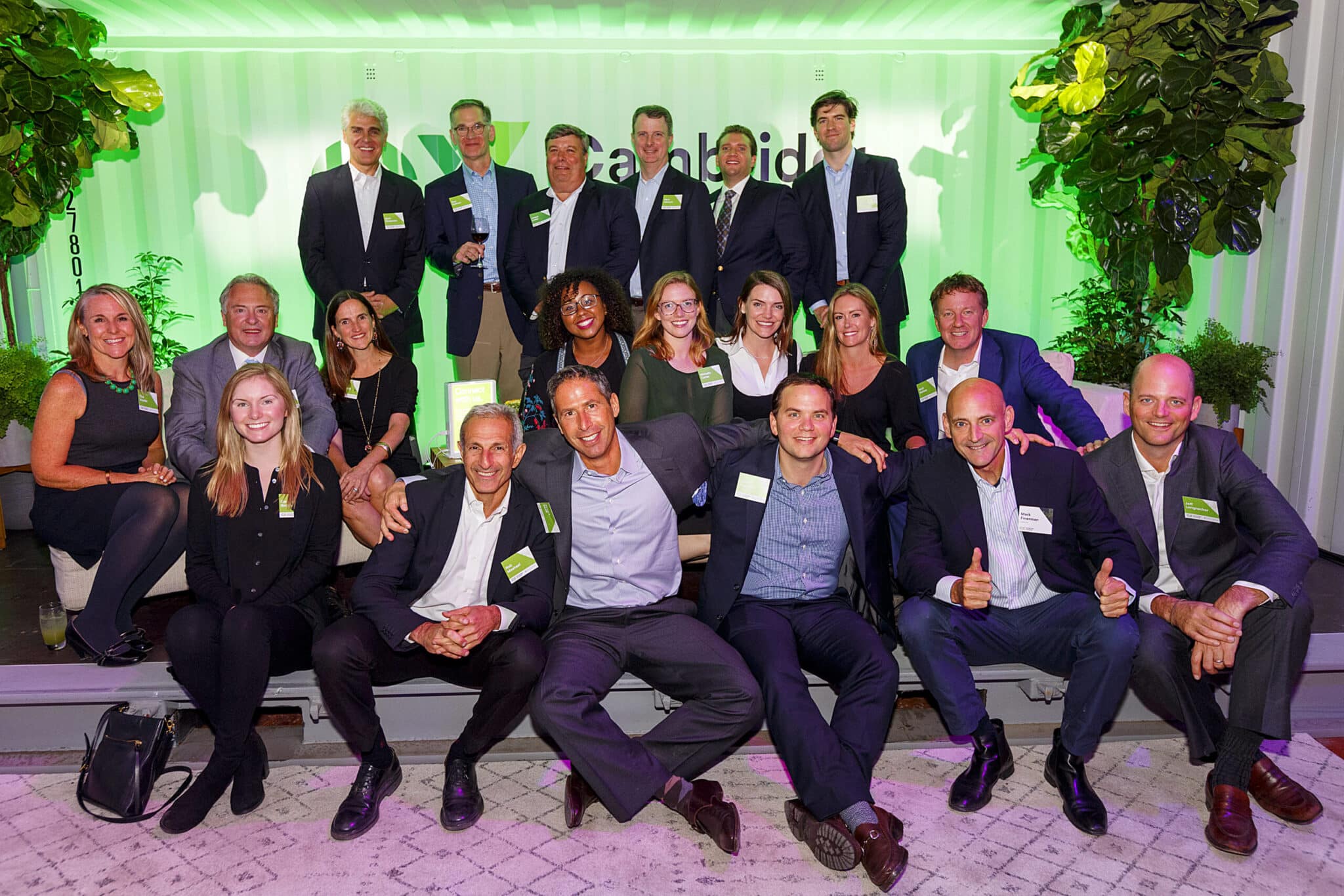 Group photo of Cambridge Crossing event attendees in front of branded backdrop and foliage