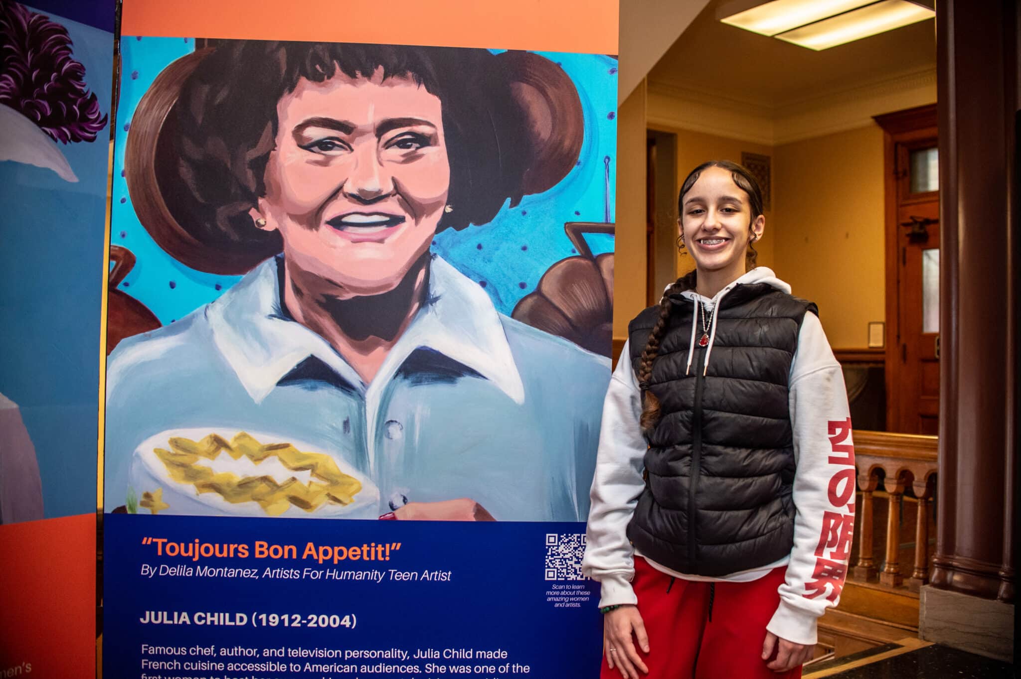 Student stands proudly beside Harriet Jacobs mural at Cambridge HerStory exhibition display
