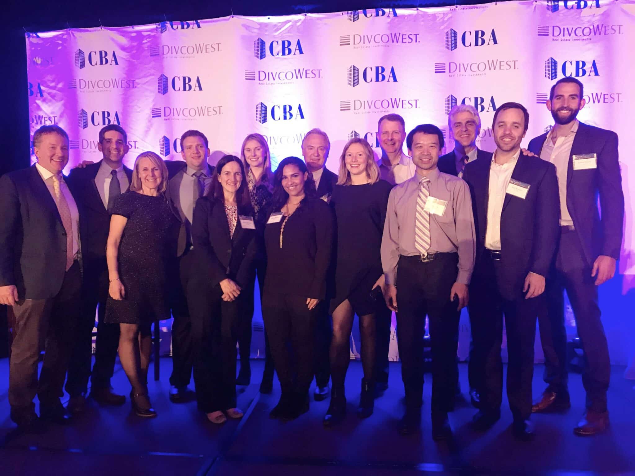 Group photo of CBA and DivcoWest team members at awards event under purple stage lights