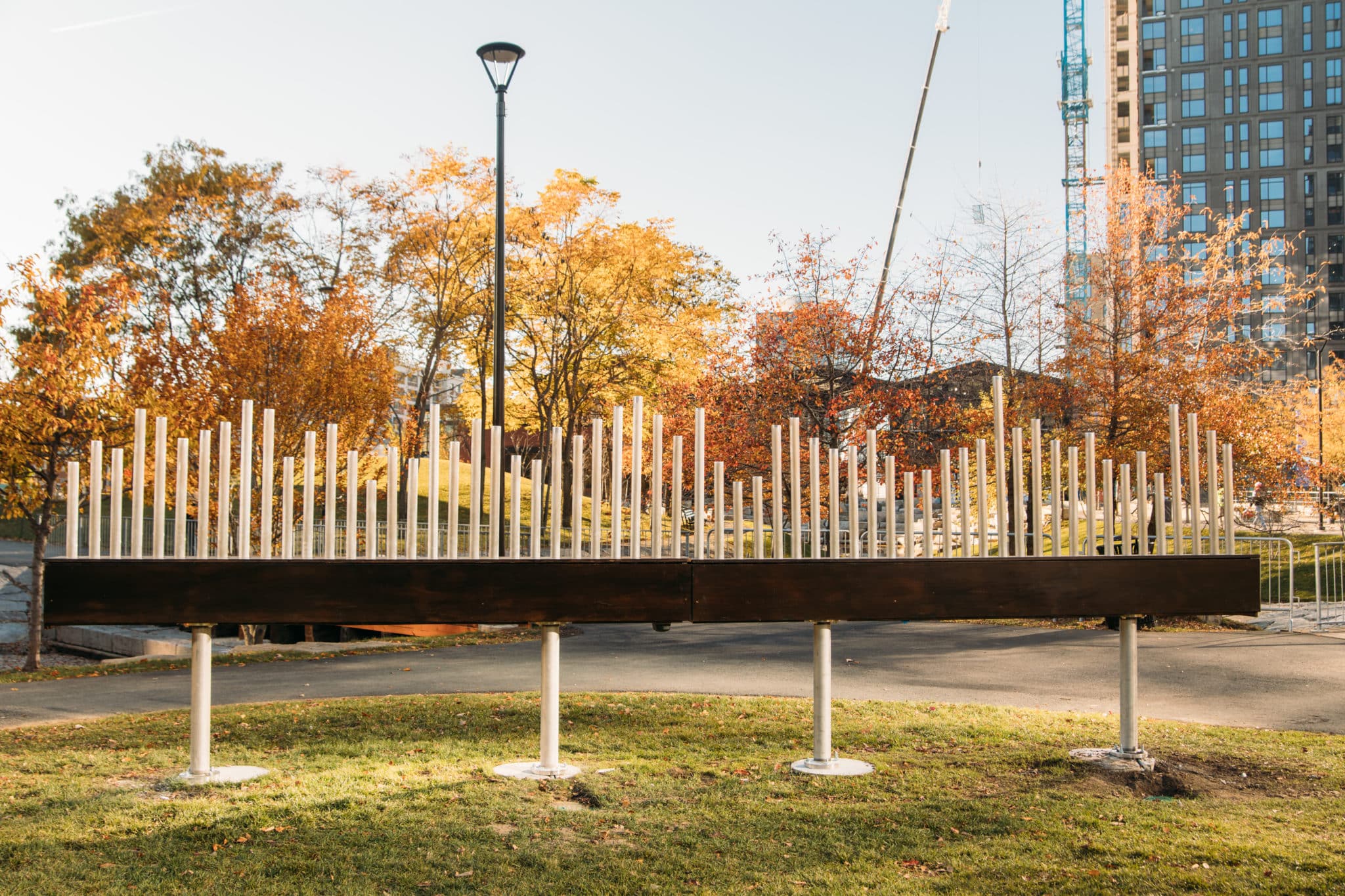 Art installation of various height metal pipes displayed on green grass in public urban park