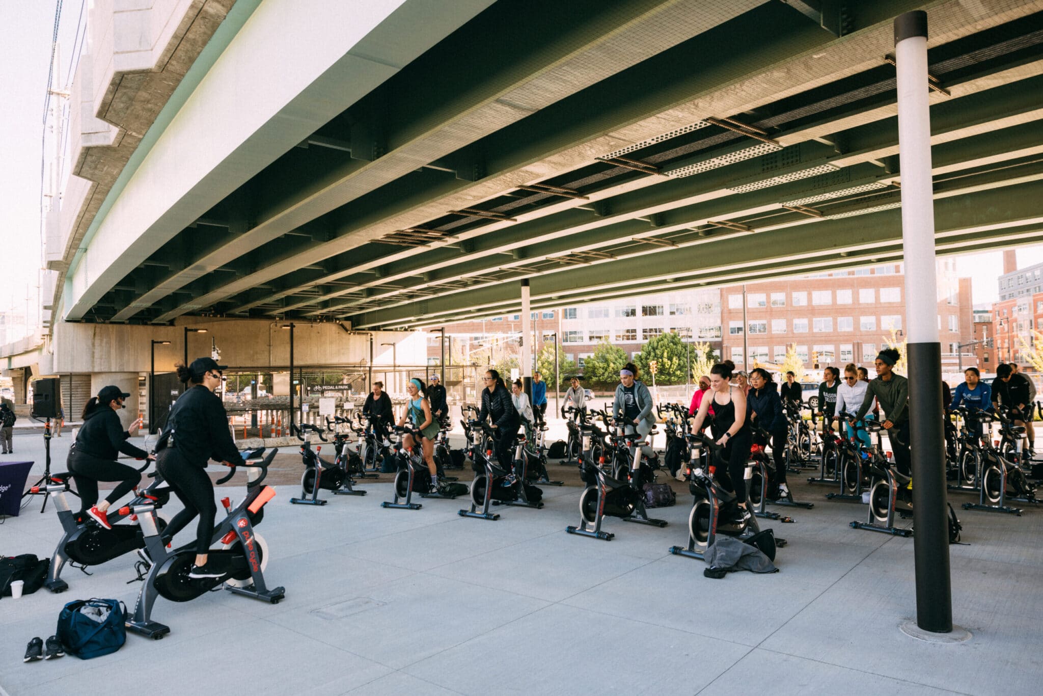 Dozens of riders spin on stationary bikes in shaded open-air workout session