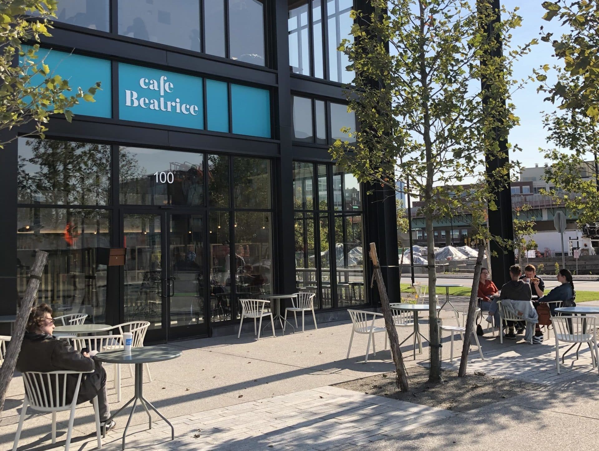 Café Beatrice patio with guests seated at tables beneath trees enjoying sunny afternoon