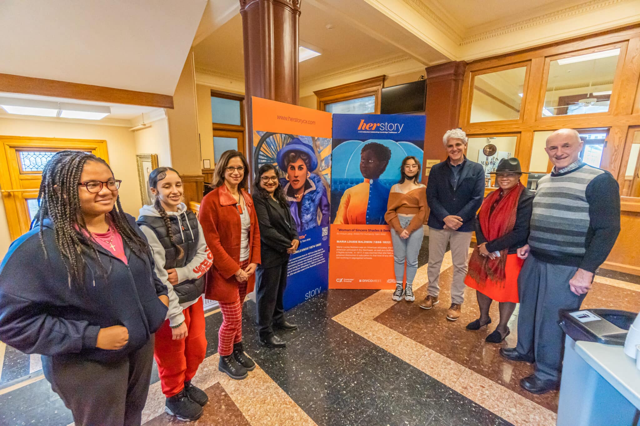 Group gathered around HerStory murals celebrating impactful women at Cambridge indoor event