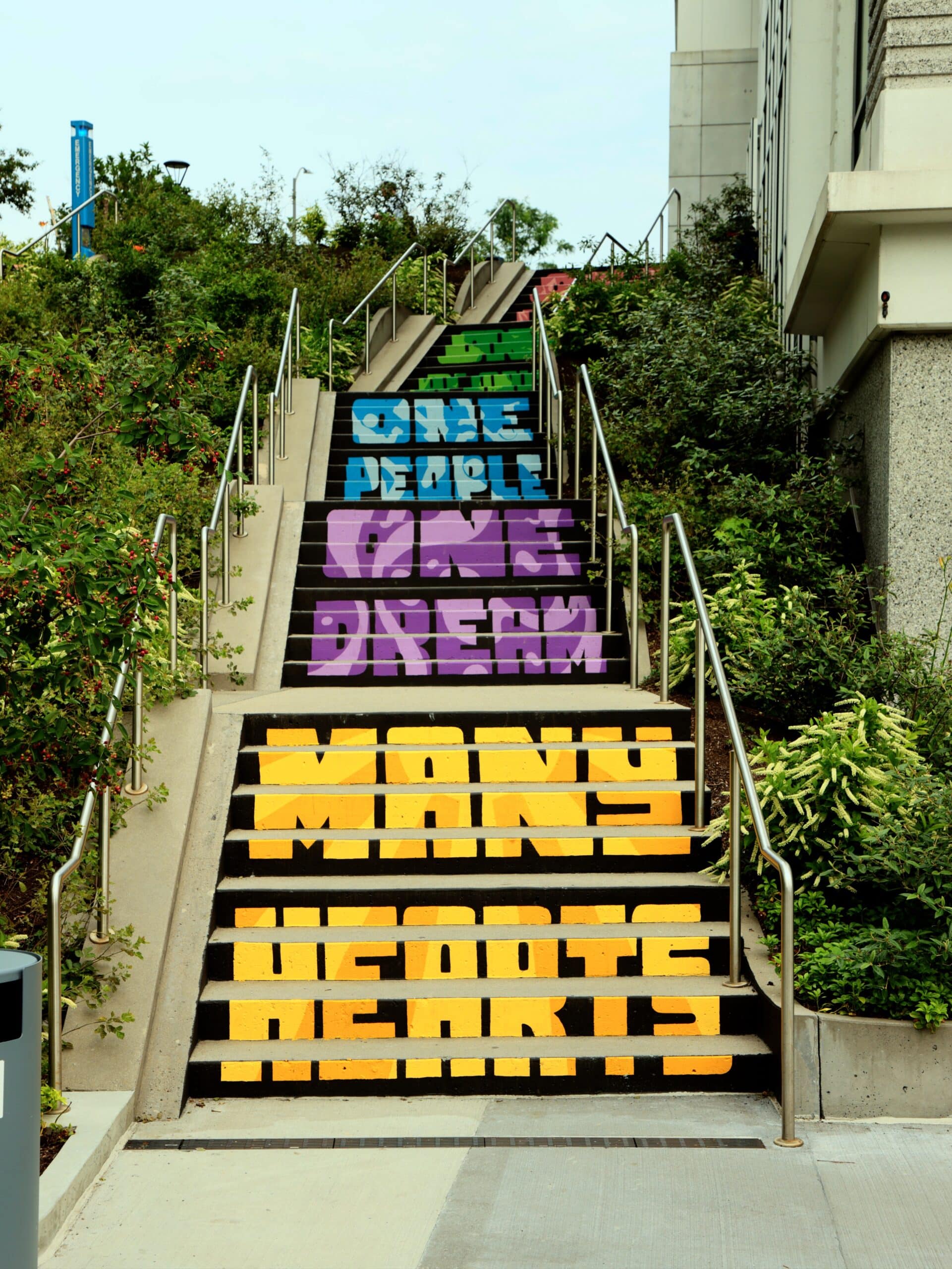 Inspirational mural on steps reads One People, One Dream, Many Hearts in colorful typography