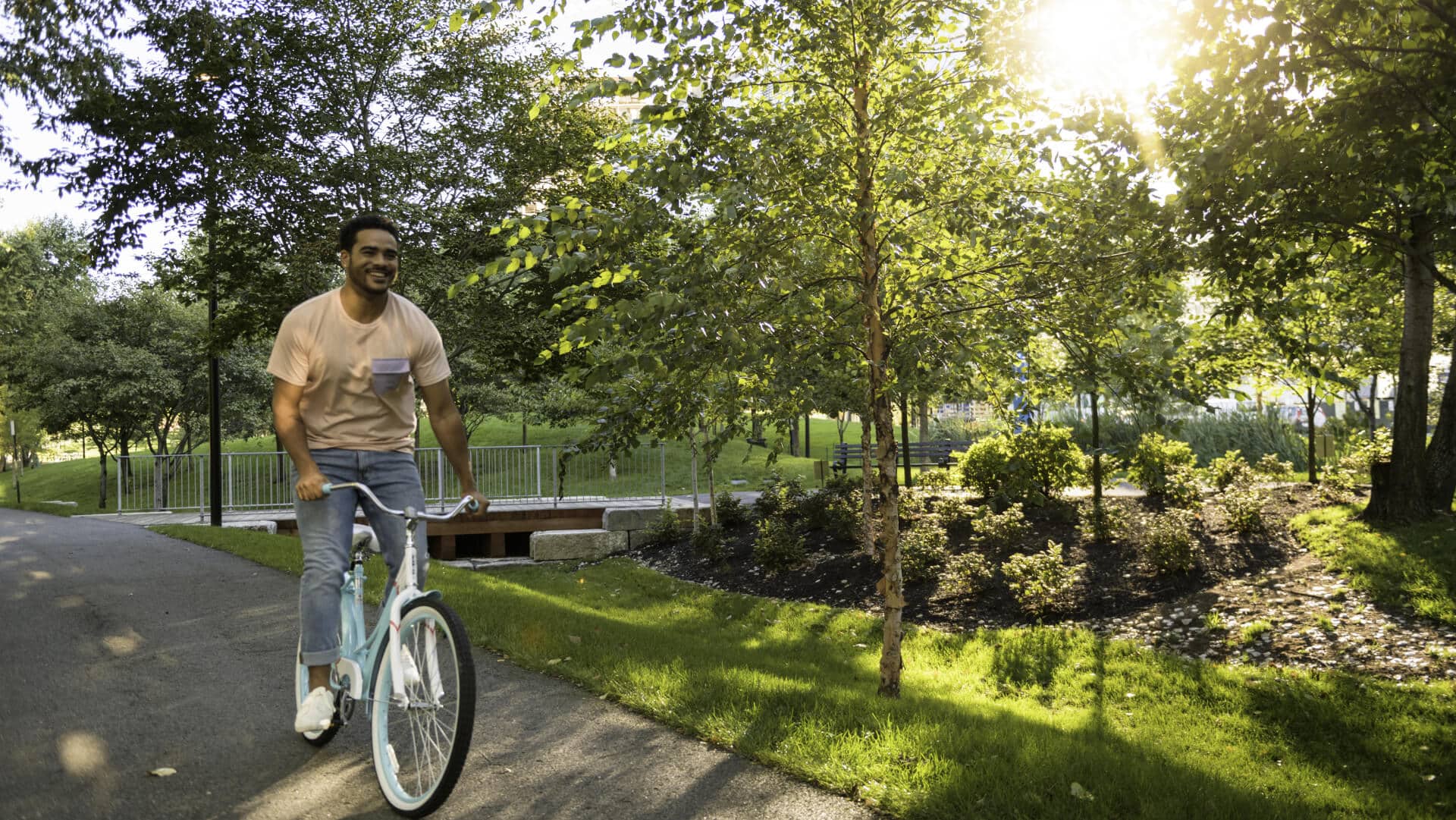 Man joyfully biking on a sunny green park trail lined with trees and landscaping