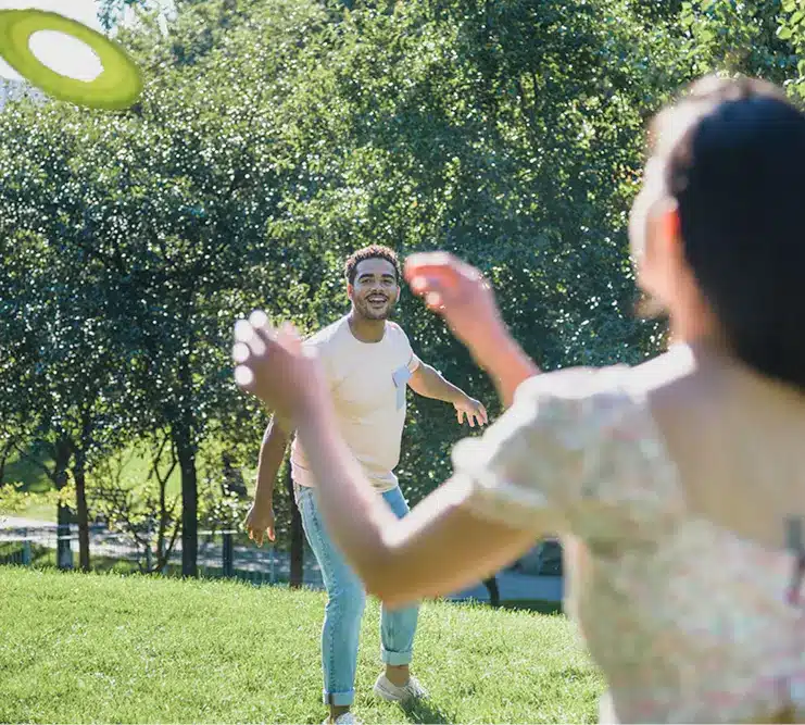 Young man and woman playing frisbee on sunny green lawn surrounded by trees in park