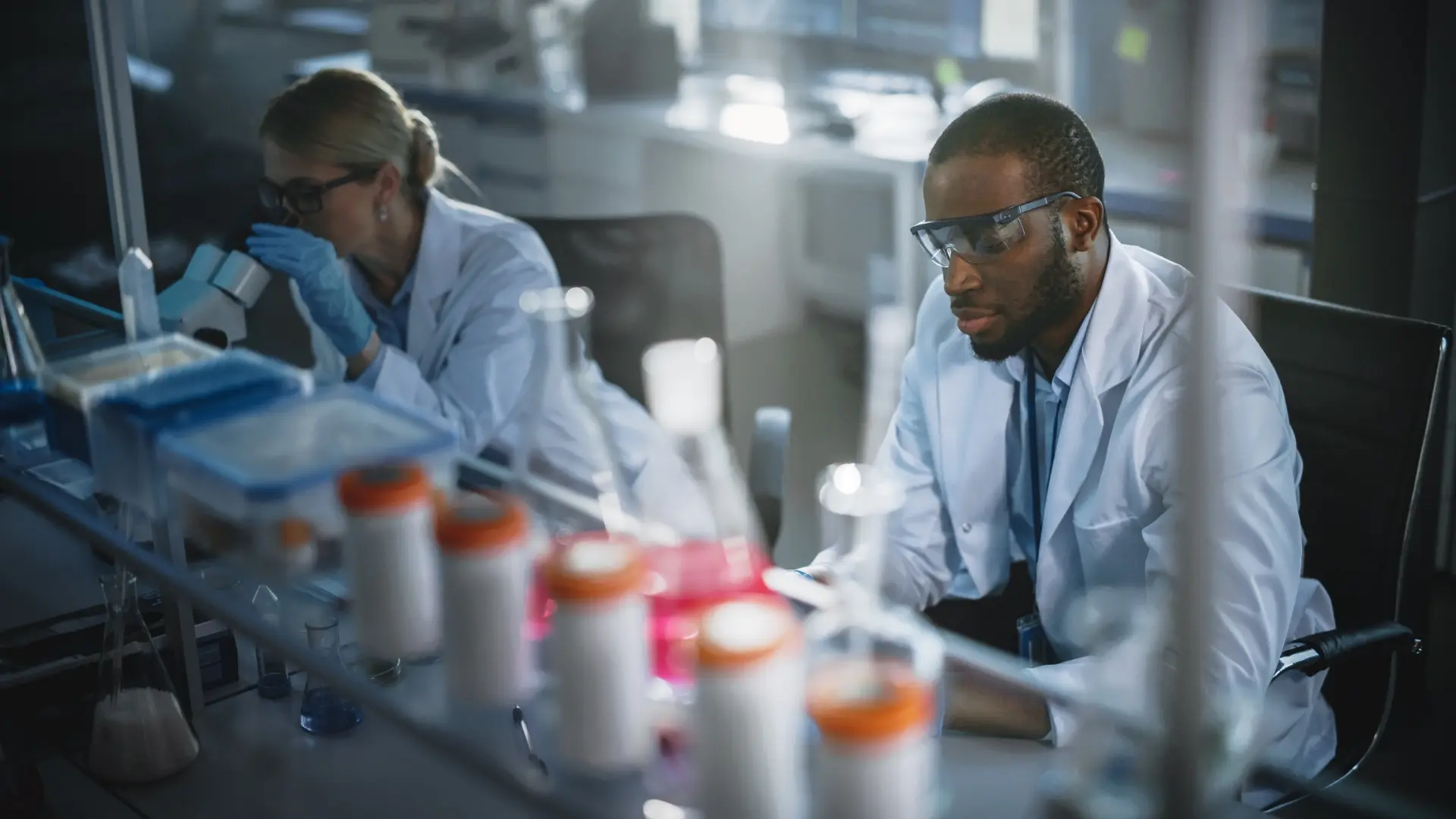Two scientists wearing lab coats conducting research in laboratory surrounded by scientific glassware