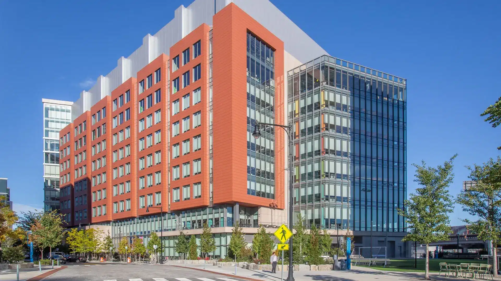 Red and silver mid-rise building with vertical fins anchors urban campus on sunny day