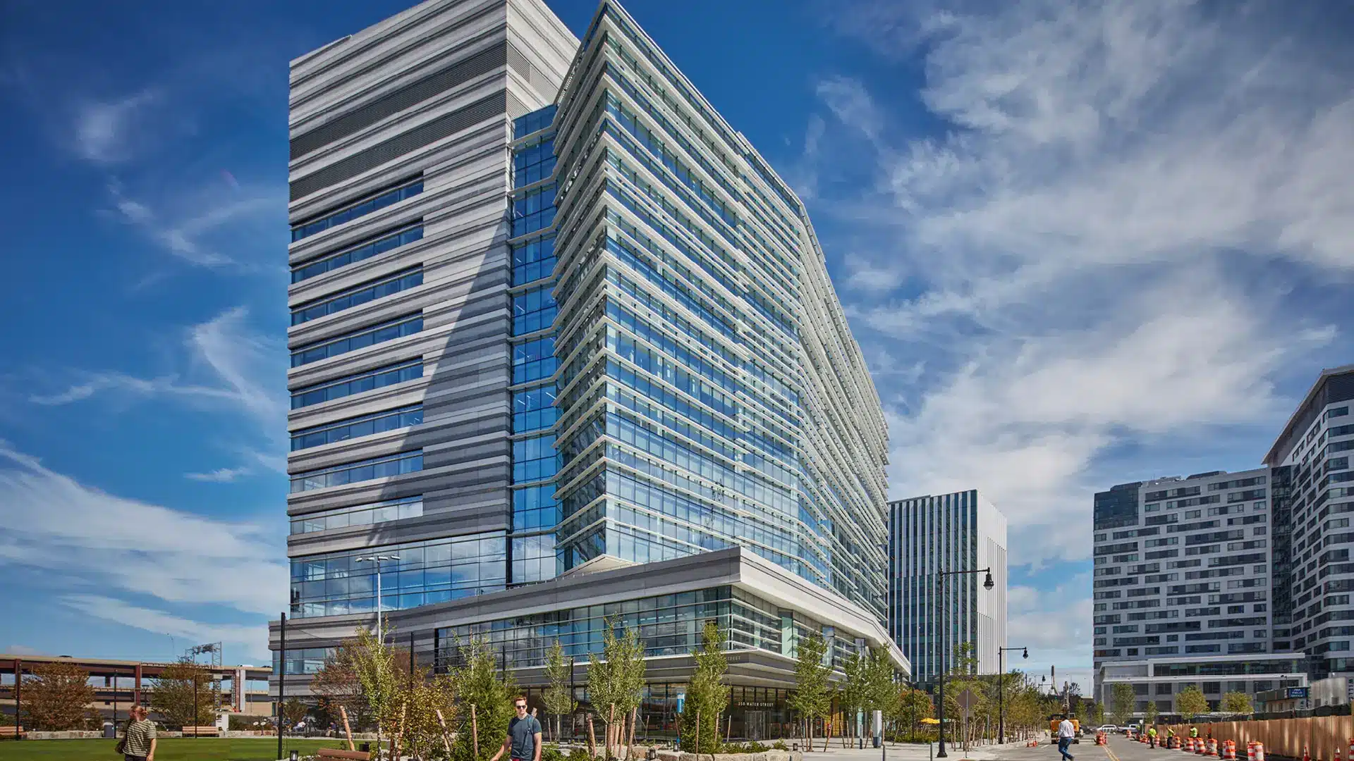 Angled view of glass and metal office tower featuring tiered facade and street-level greenery