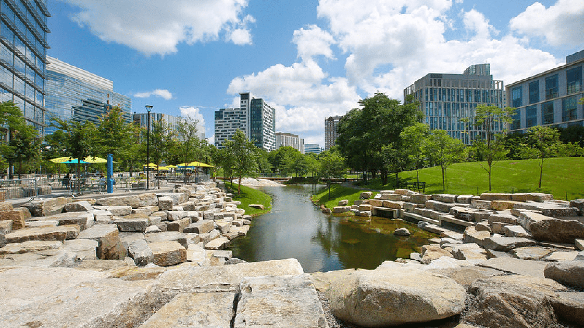 Stream lined with large stone boulders flows between modern office buildings and green lawns