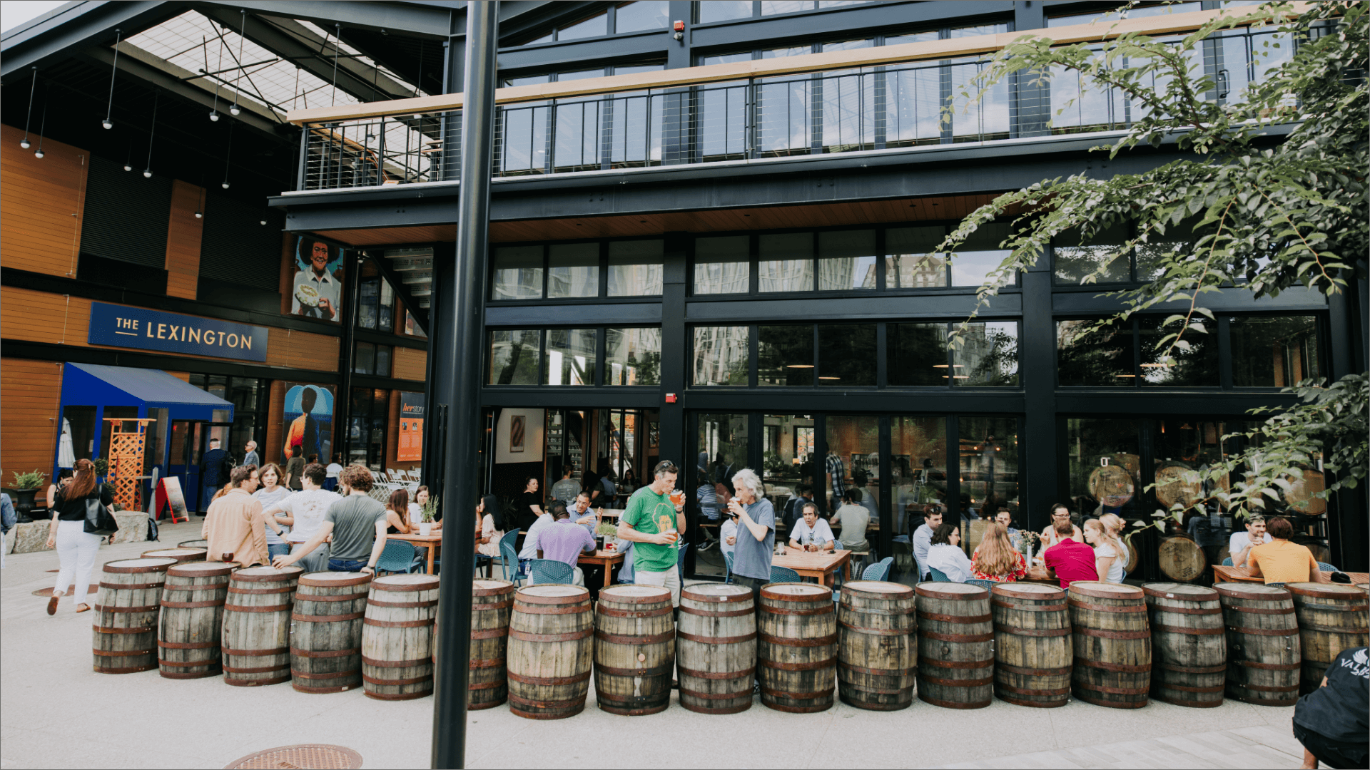 LampLighter Brewery - People dining outside The Lexington restaurant surrounded by reclaimed barrel seating and modern design