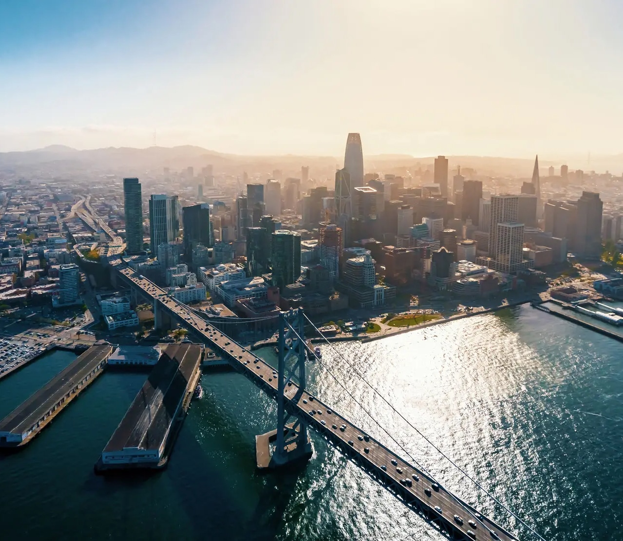 Aerial city view with San Francisco skyline, Bay Bridge, and waterfront reflecting late afternoon sun
