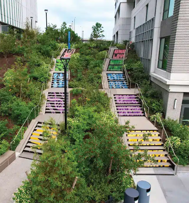 Colorful staircase murals leading through green hillside between modern buildings in cityscape
