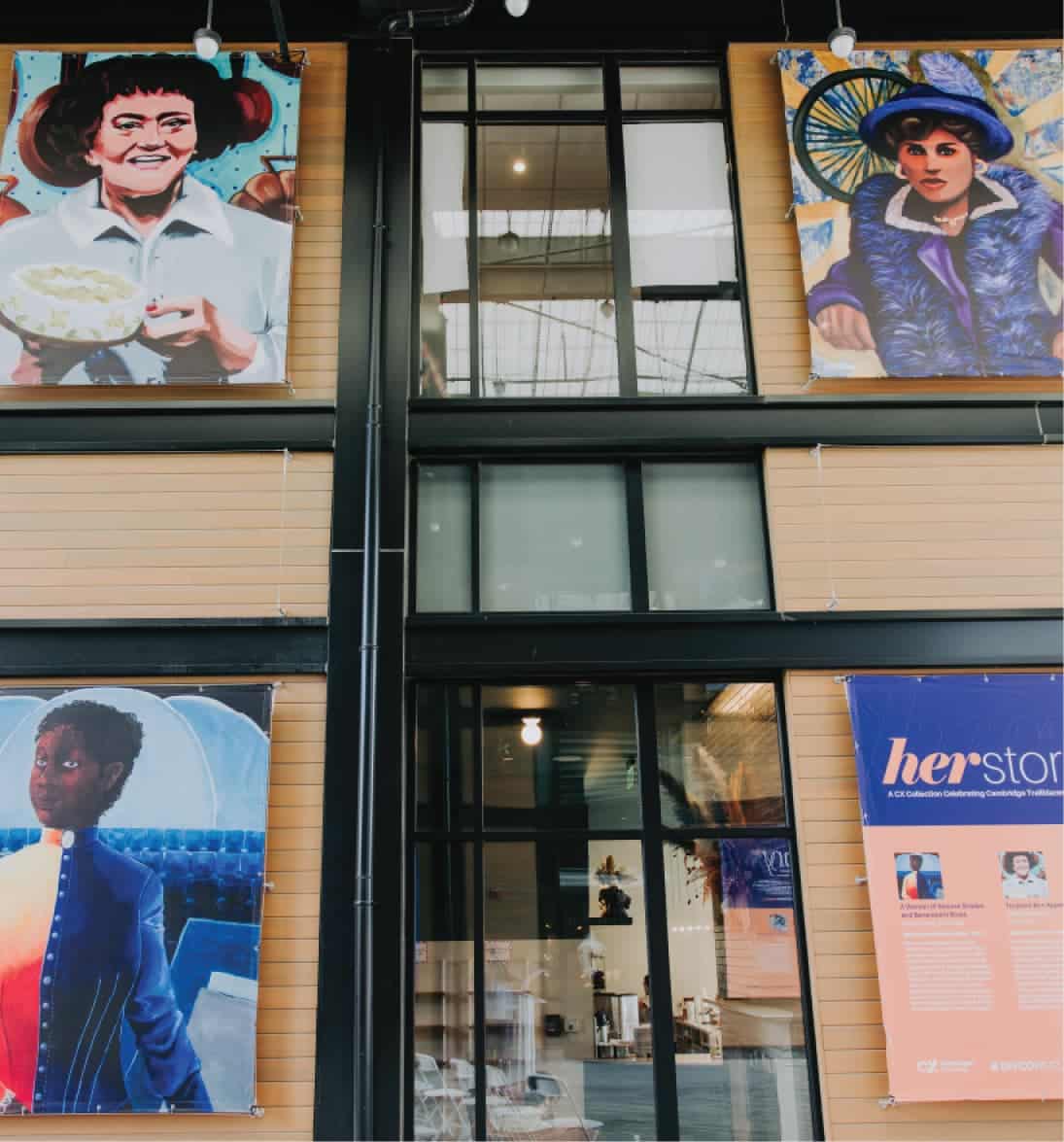 Gallery wall featuring multiple women-focused artworks with banner for “Herstory” collection exhibition