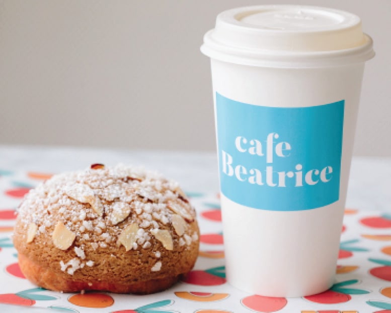 Cafe Beatrice coffee cup with almond pastry on colorful patterned surface, bright and inviting
