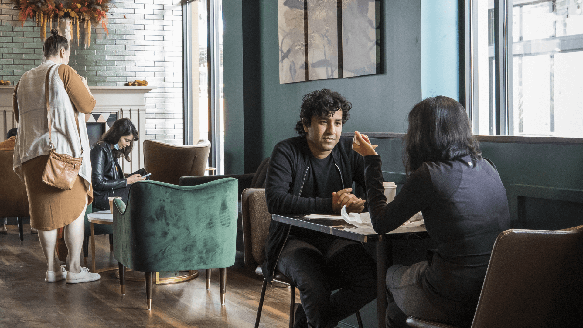 Cozy café interior with teal seating, people conversing and working at marble-top tables