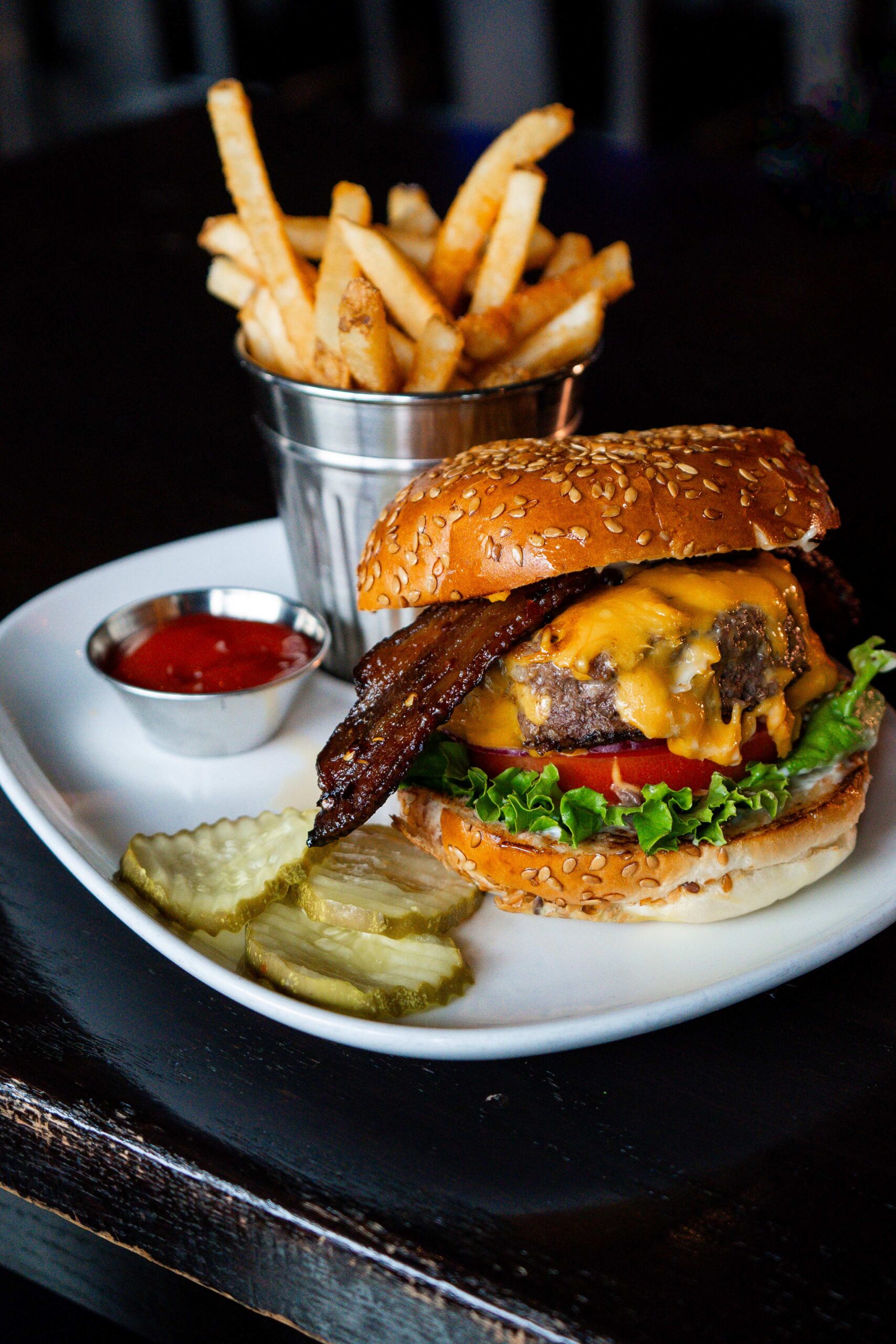 Juicy bacon cheeseburger on sesame bun served with fries, pickles, and ketchup in stylish plating