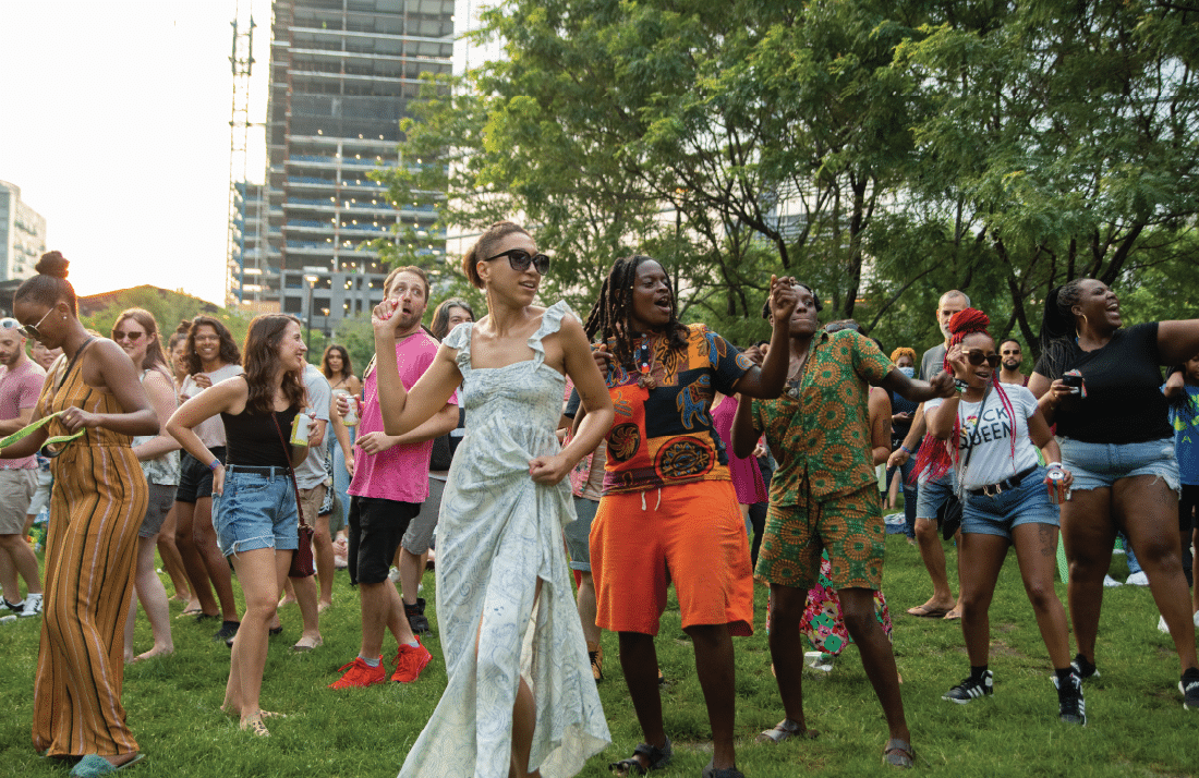 Lively public celebration with people dancing, laughing, and gathering on a grassy lawn