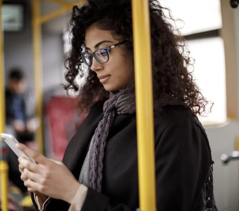 Woman with scarf and glasses reading phone during public transportation ride through city