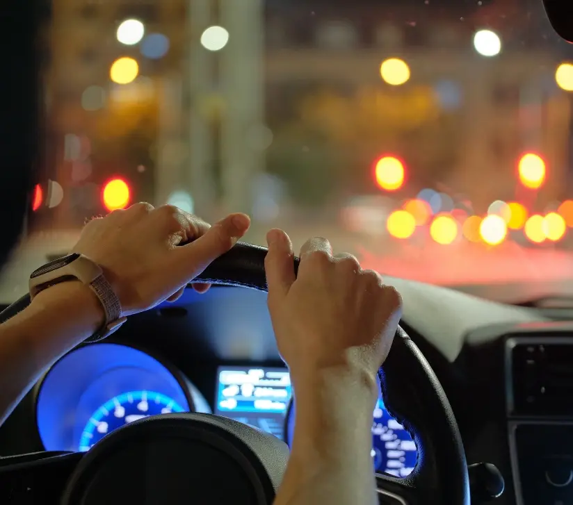 Hands gripping steering wheel during night drive with city lights blurred in the background