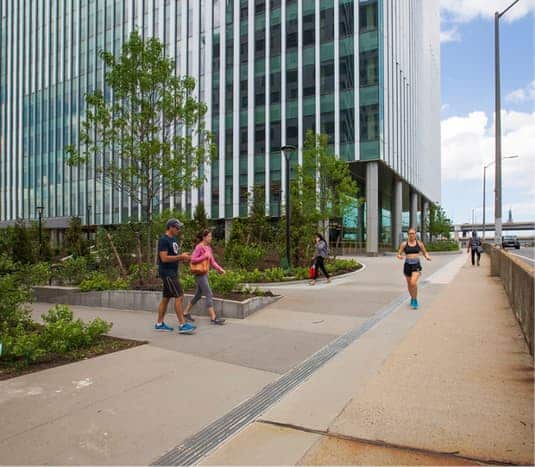 People walking and jogging on landscaped pathway beside modern glass office building downtown