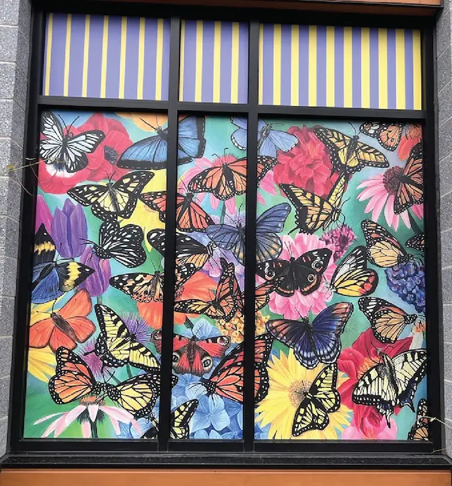 Colorful butterfly mural on window display with vibrant flowers and bold striped awning