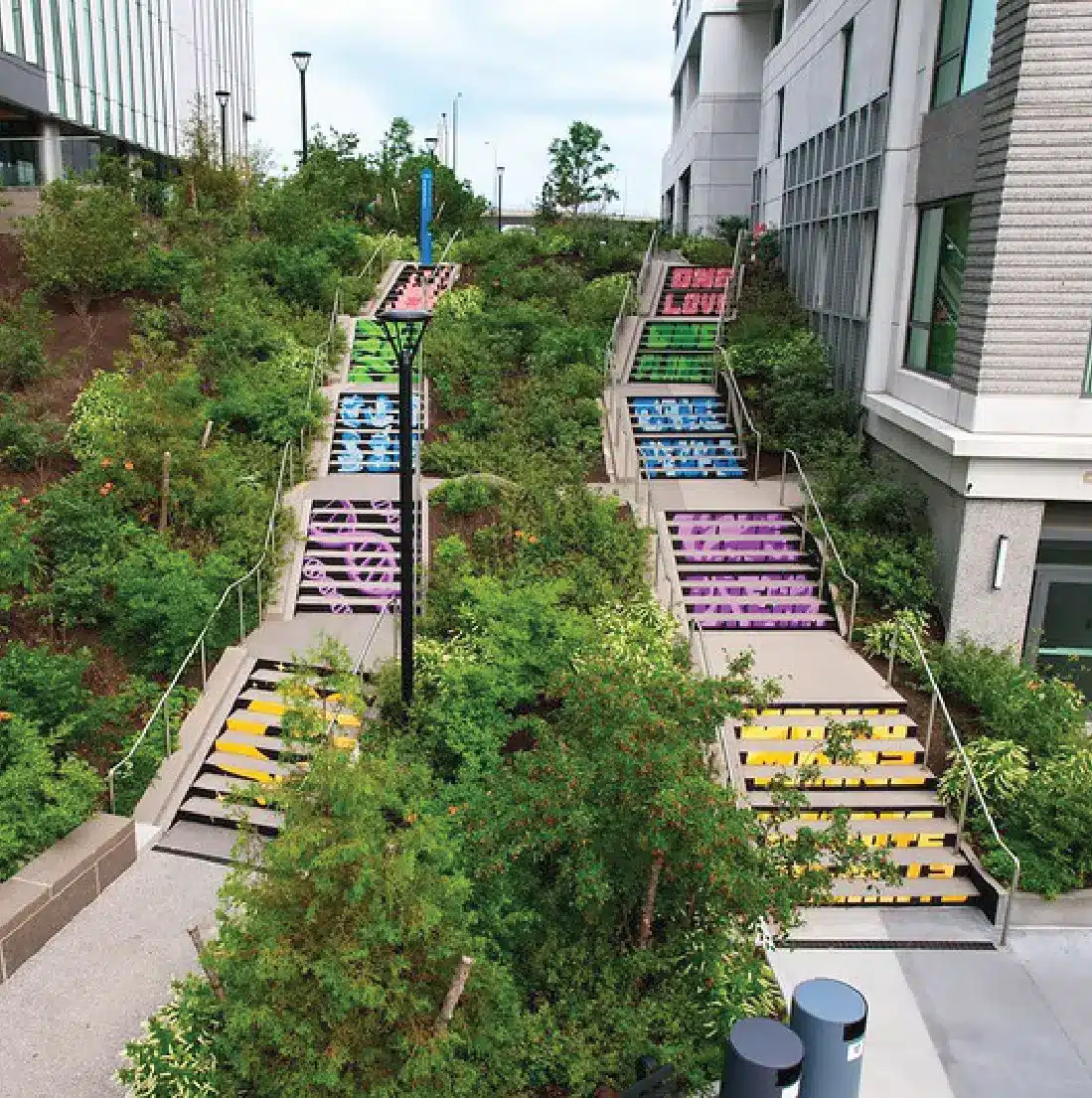 Colorfully painted staircases reading One Love nestled in greenery between modern urban buildings