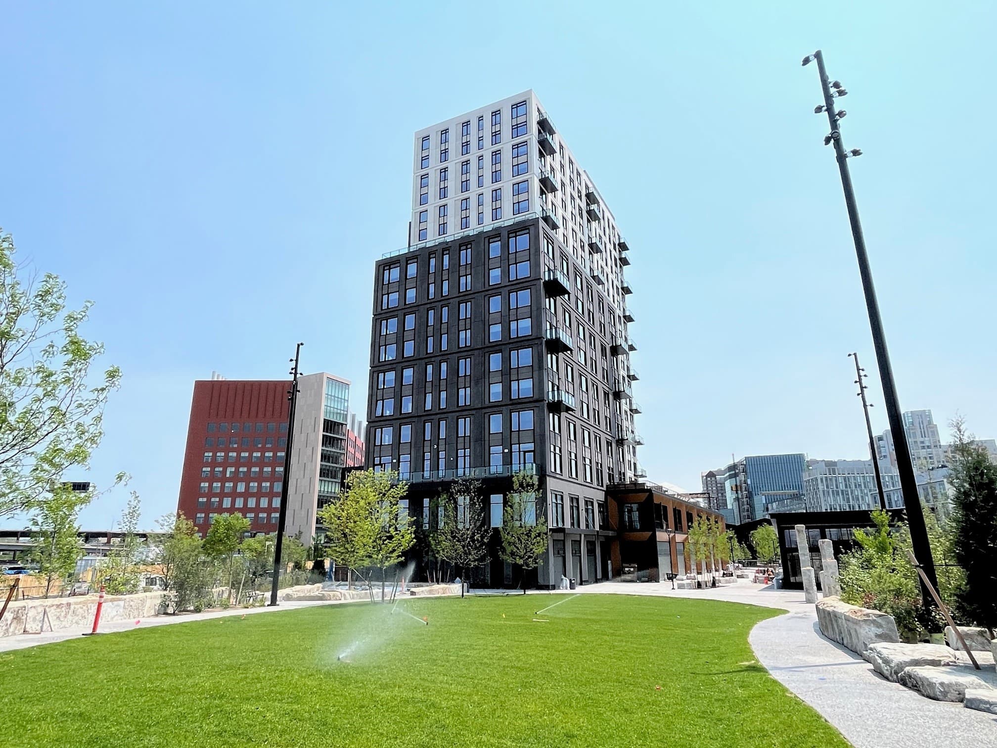 Mixed-use residential development featuring dark facade, expansive windows, and urban green space