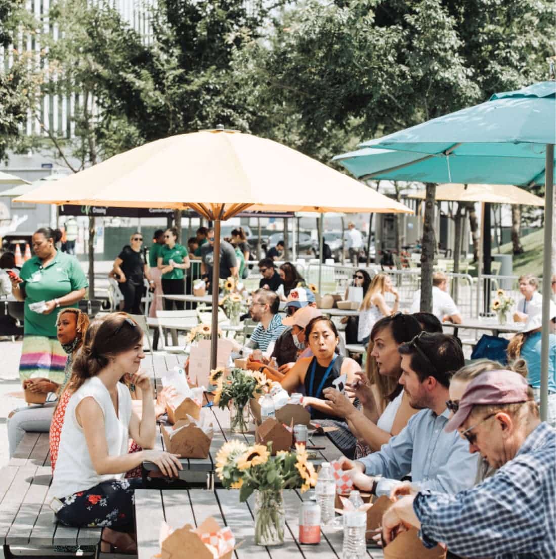 People enjoying lunch under umbrellas at a lively outdoor community picnic gathering