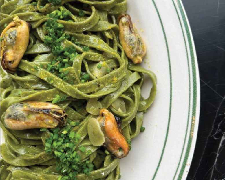 Plate of green spinach tagliatelle pasta topped with mussels and fresh chopped chives