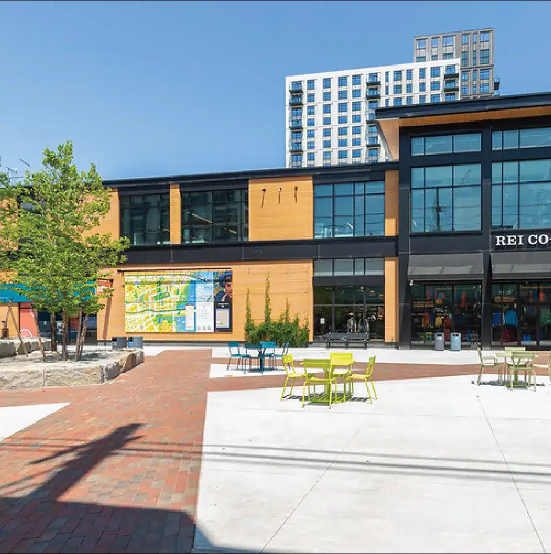Outdoor shopping plaza with REI store, map signage, and modern apartment building in background