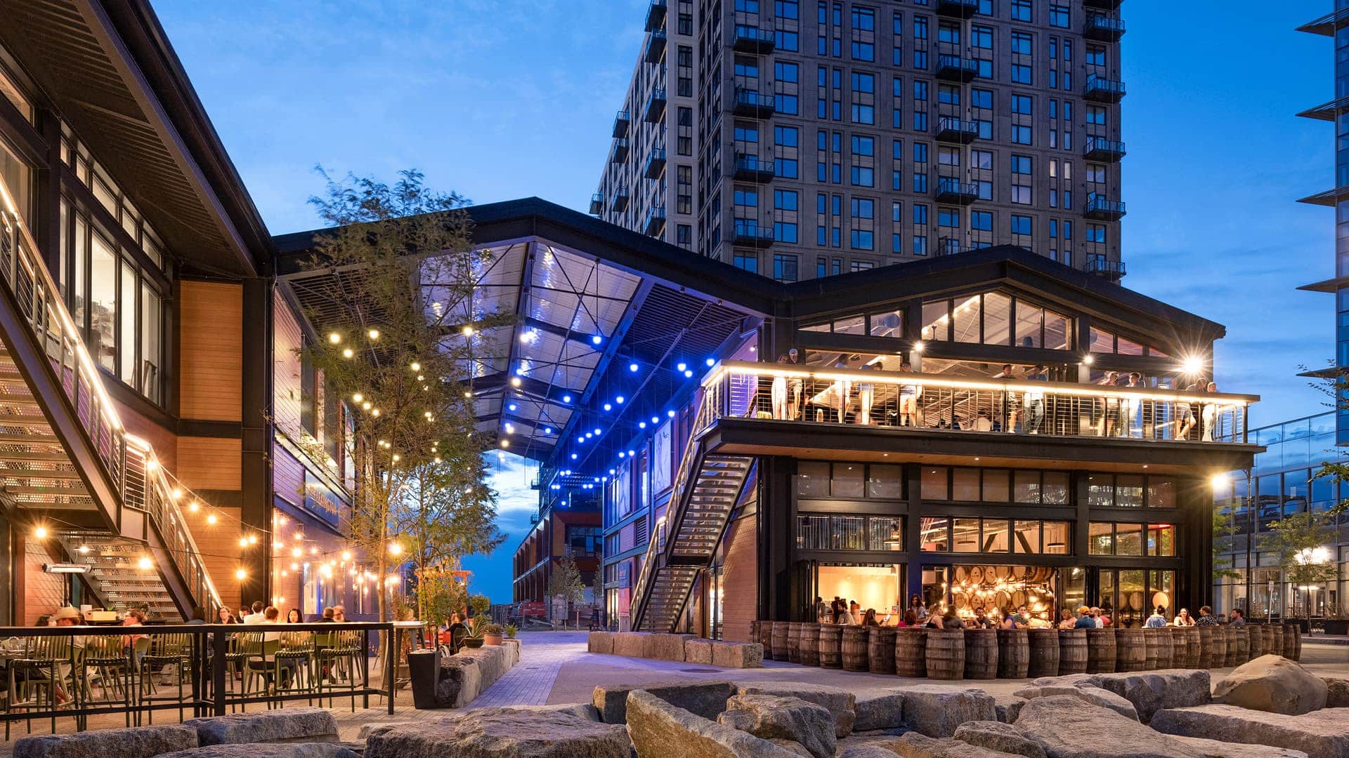 Evening at The Shed with people dining under string lights beside modern two-story restaurant