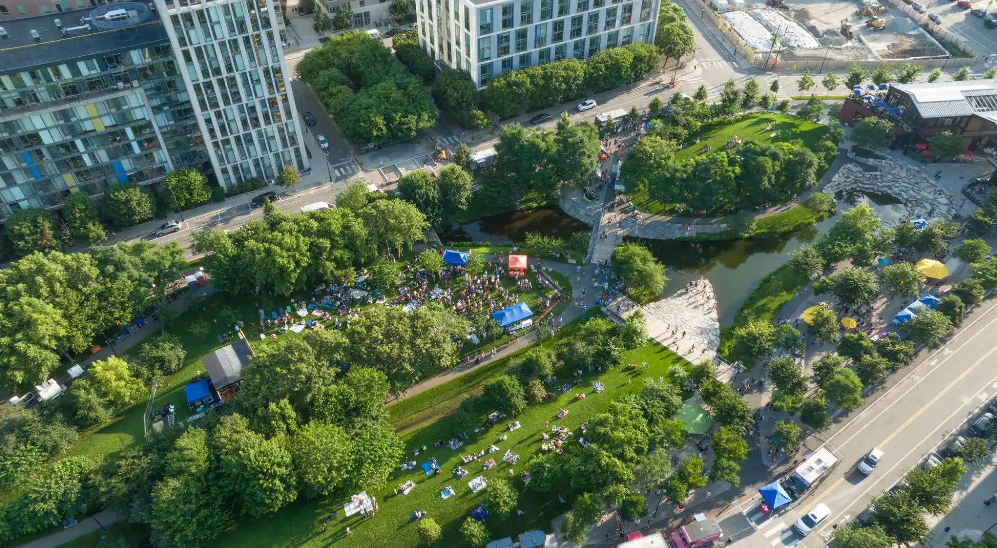 Aerial summer event in urban park with food trucks, picnic blankets, and shaded gathering tents