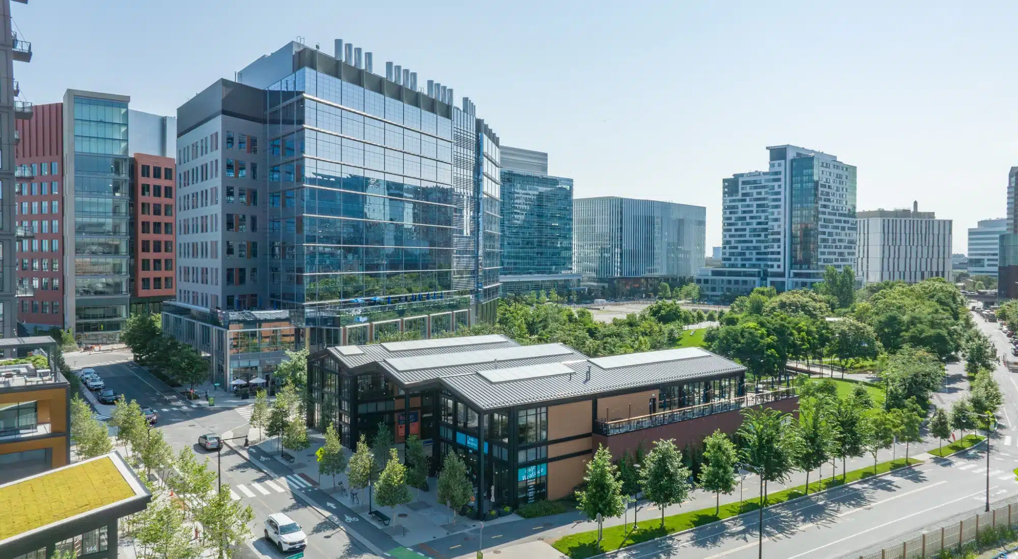 Modern cityscape with glass buildings and park-front commercial center shown on sunny afternoon