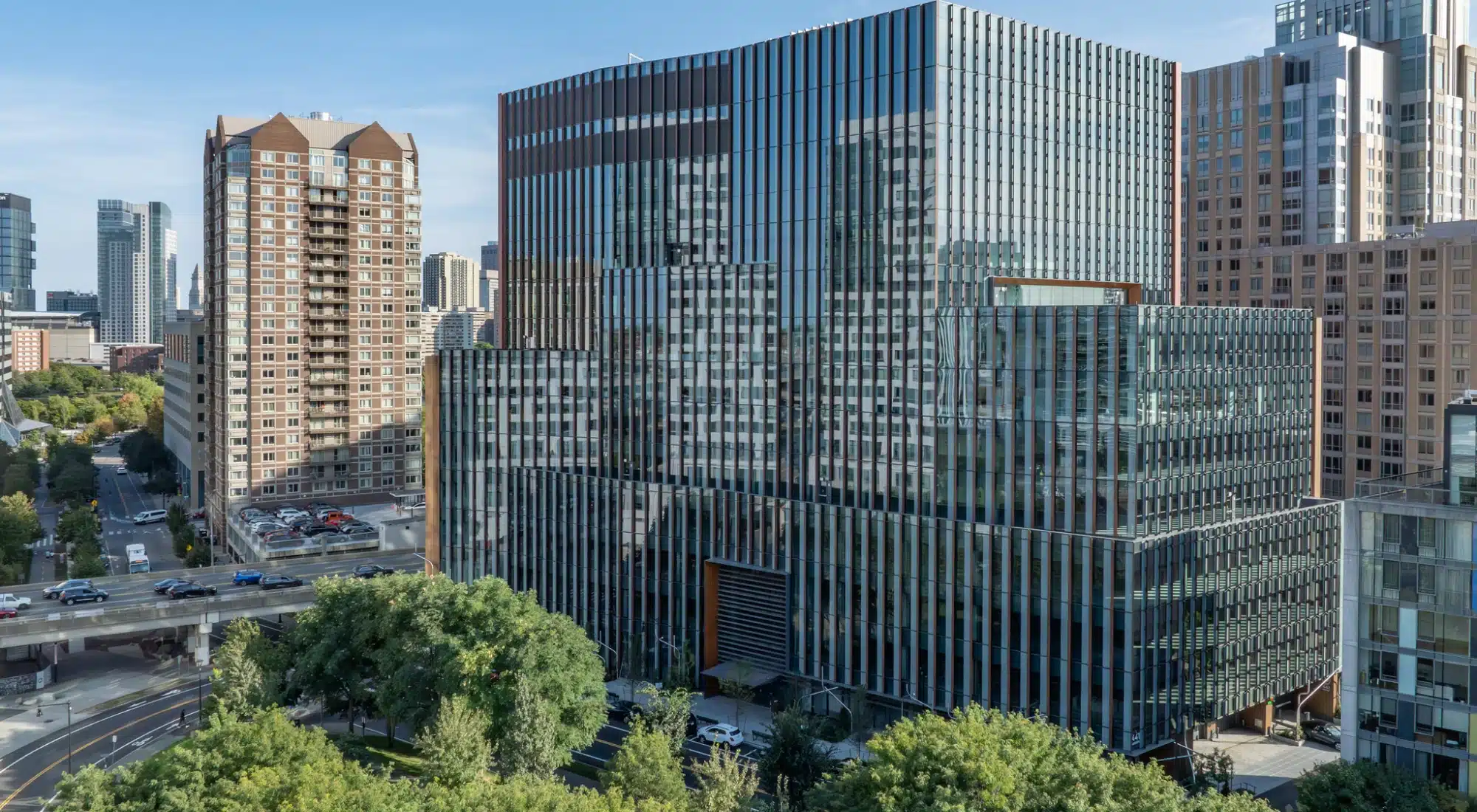 Glass office tower with vertical fins reflecting city skyline and adjacent high-rise apartment buildings