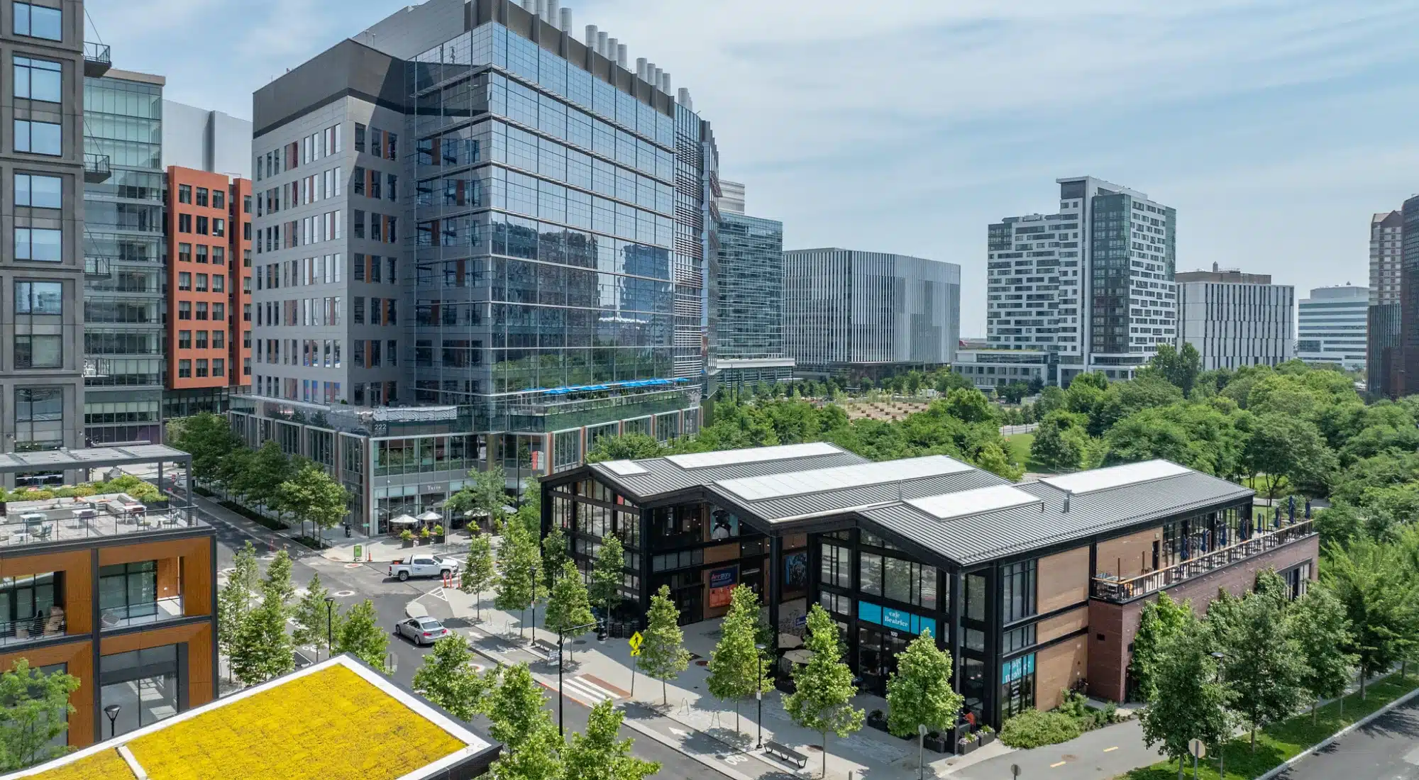 Cluster of modern buildings with tree-lined sidewalks and cafe storefront in urban mixed-use district