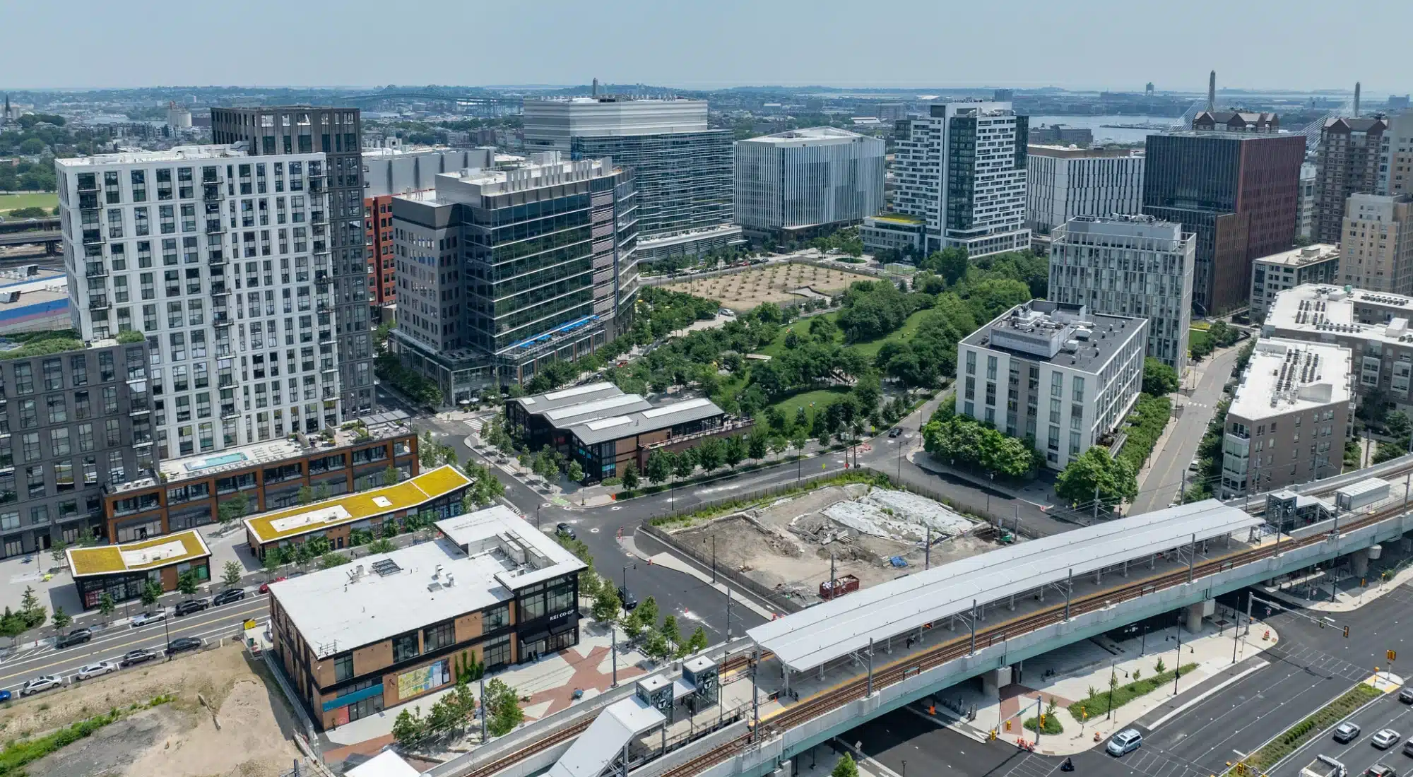 Wide aerial shot of urban district showing transit station, new developments, and surrounding greenery